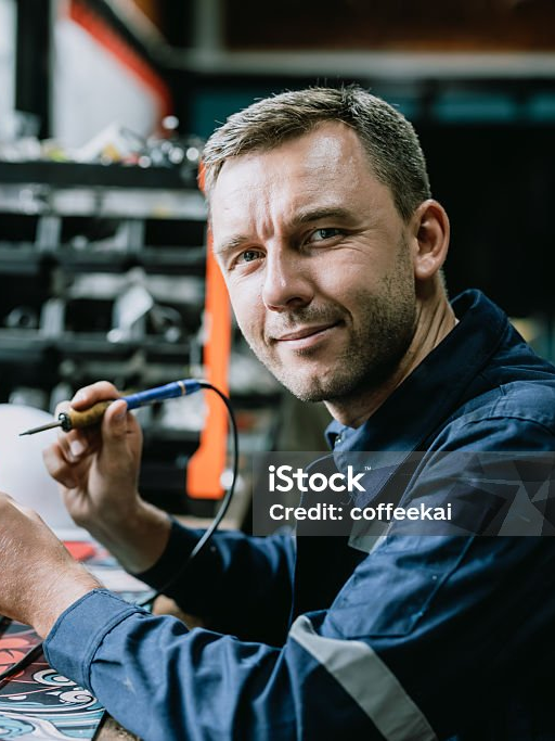 Elektriker an seinem Arbeitsplatz, er blickt von einer Platine auf