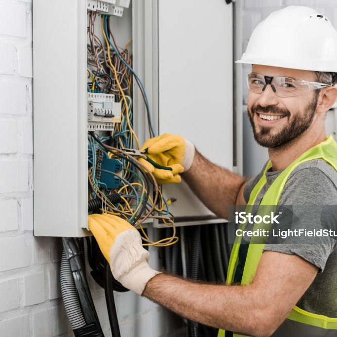 Elektriker mit Helm und Warnweste verdrahtet einen offenen Zählerschrank