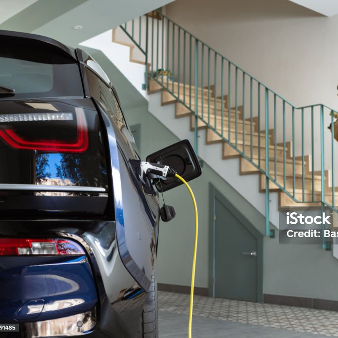 Gelbes Ladekabel steckt am Heck eines Autos in einer überdachten Einfahrt