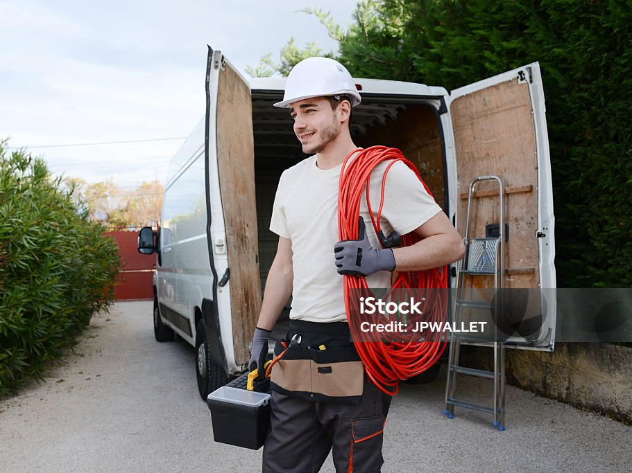 Elektriker mit einer Kabelrolle vor seinem geöffneten Transporter